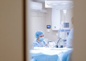 View of a surgeon working in an operating room through a door window, emphasizing medical precision.