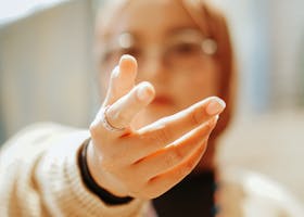 A woman wearing a hijab offers her hand with a blurred background, capturing intimacy.